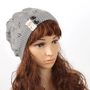 Close-up of gray knitted beanie with leaf pattern, lace patch, and button detail.