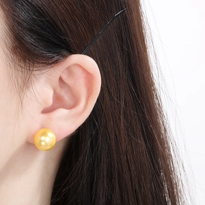 Close-up of a large golden pearl stud earring worn by a model with dark hair