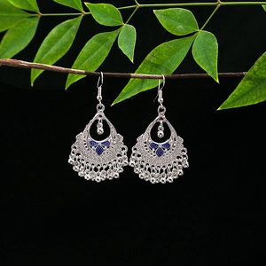 Detail of silver ethnic tassel earrings with blue enamel hanging on a green leaf branch
