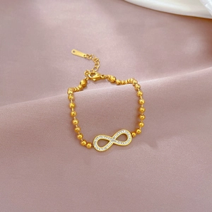 Detail of gold infinity charm bracelet with white zircon inlay on silk background