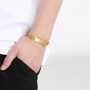 Detailed view of a gold stainless steel Cuban ID bracelet on a model's wrist with flat plate