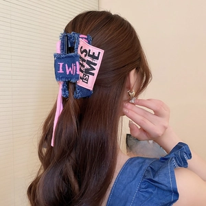 Detail view of a denim bow hair claw clip in blue and pink worn on a woman's hair