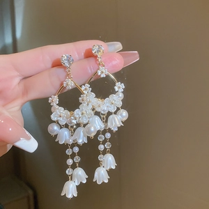Elegantes pendientes de lirio de los valles con flores blancas, perlas y borlas doradas