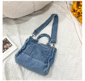 Flat lay of blue denim tote bag with adjustable strap and handles on white fabric