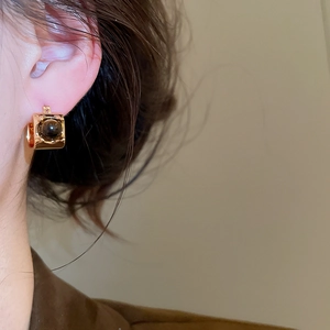 Close-up of gold-plated tiger eye stone round earrings worn on a female model