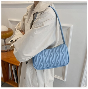 Detail of light blue crossbody bag with wavy quilted texture worn by model