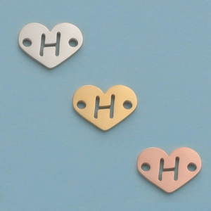 Macro detail of 12mm mirror-polished steel heart pendants with H cutout in 3 colors