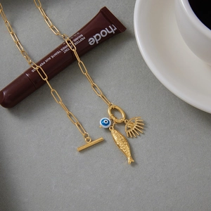 Detail view of gold titanium evil eye necklace with fish charm on a textured surface