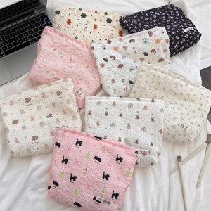 Flat lay of multiple quilted floral and cartoon cosmetic bags on a white bed sheet