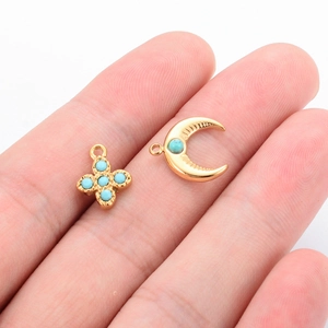 Golden clover and moon pendants with turquoise stones shown on a finger for size