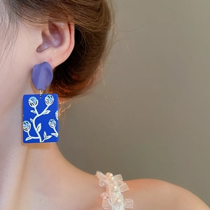Macro shot of rectangular blue floral drop earrings with purple petal accents on a model