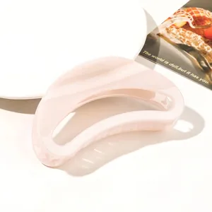 Macro detail of a high-gloss light pink crescent hair claw clip on a white plate