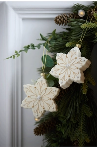 Detail of cream white snowflake ornament with gold patterns on a pine wreath branch
