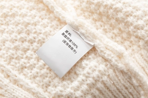 Dettaglio ravvicinato della maglia color crema con etichetta in 100% fibra di poliestere