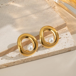 Elegant gold oval pearl stud earrings on a beige travertine stone with natural lighting