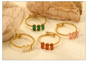Detail of four gold twisted rings with colorful rectangular zircons on a rock surface