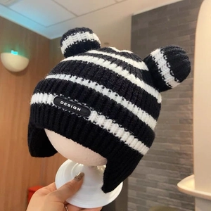 Close-up of black and white striped knit earflap hat with cute pom-pom ears for infants
