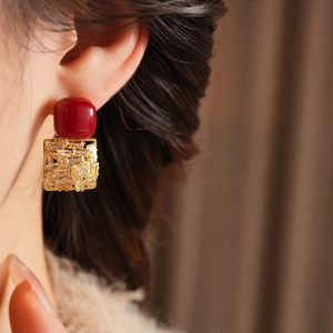 Close-up of elegant square zircon earrings with red resin on gold base on model