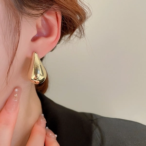 Close-up of large golden teardrop earrings with high-polish finish on model