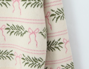 Detail of cream knit sweater showing festive green pine and pink bow jacquard patterns