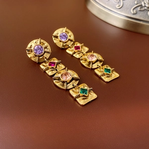 Vintage gold drop earrings with colorful gemstones and long tassel design on leather texture