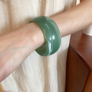 Detail of a wide light green acrylic bangle with marble texture worn by a model