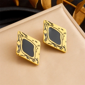 Detail of gold-plated rhombus earrings with black enamel inlay on a beige display mat