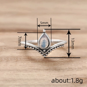Anello a V in argento con pietra di luna a goccia e bordo perlato su sfondo di legno