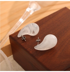 Vue macro de boucles d'oreilles gouttes blanches effet marbre sur une boîte à bijoux en bois