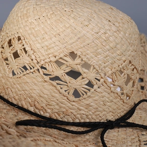 Detail of hand-woven straw sun hat showing hollow-out pattern and black cord texture