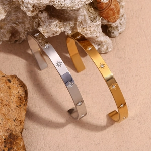 Detailed view of gold and silver open bangles with starburst patterns on beach rocks