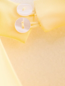 Détail de la texture satinée jaune avec deux boutons en résine blanche sur la manche