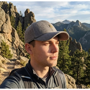Detail of grey herringbone baseball cap with gold metal R logo in outdoor nature setting