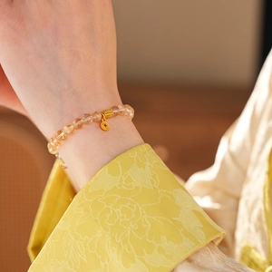 Detail of beaded crystal bracelet with gold coin charm on silk sleeve background