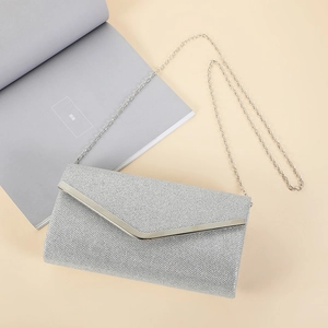 Silver envelope clutch bag with gold trim and chain strap on a beige background