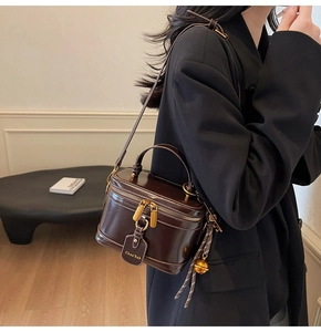 Model wearing dark brown box bucket bag with gold hardware and side strap detail