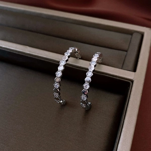 Gros plan de boucles d'oreilles créoles en C argentées avec motif hexagonal serti