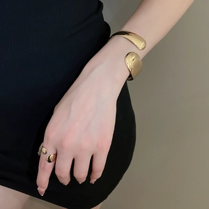 Detailed close-up of shiny gold-plated fluid organic open cuff bracelet and matching ring