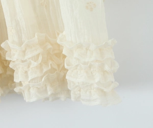 Détail de robe blanc crème avec volants superposés, broderie florale et tissu en mousseline