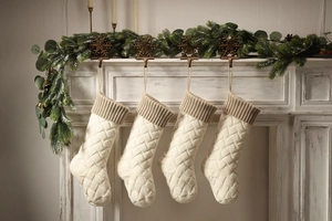 Close-up of four beige knitted Christmas stockings with brown cuffs on a festive fireplace
