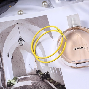 Détail macro de grandes créoles jaune mat stylisées avec parfum de luxe et perles