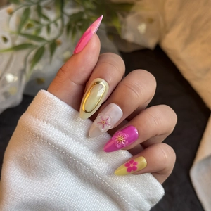 Detail of almond-shaped press-on nails featuring 3D floral accents and gold embossed lines