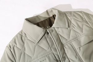 Macro shot of light grey-green quilted winter jacket showing stitching and snap buttons