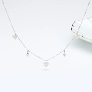 Detail of silver necklace featuring heart charms and diamond-encrusted rhombuses