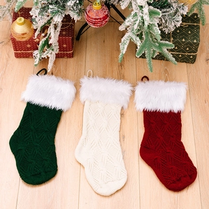 Knitted Christmas stockings in green, white, and red with faux fur trim on wood floor