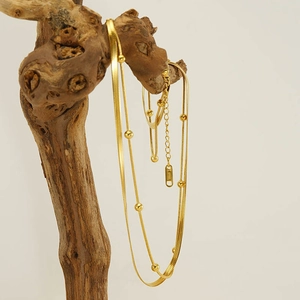 Detail of a layered golden stainless steel snake chain necklace with bead accents