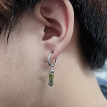 Detailed view of silver hoop earrings with green bamboo pendant on a model's ear