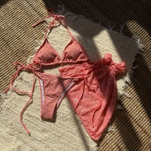 Detailed close-up of pink 3-piece lace bikini set with matching mesh sarong and gold accent