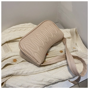 Close-up of beige shoulder bag with wavy quilted pattern on white knit fabric