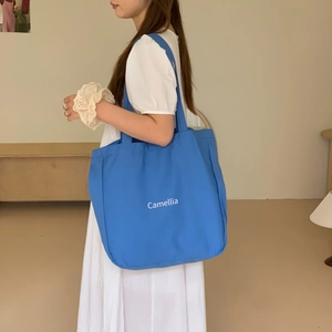 Nahaufnahme einer blauen Canvas-Tasche mit weißem Camellia-Textdruck am Model
